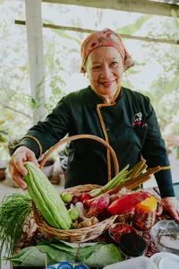 Indigenous Sabahan cook in Kota Kinabalu holding a basket of fresh greens and herbs, wearing traditional headscarf and dress