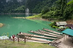 Old bamboo raft platforms and a floating jetty by a turquoise shoreline, framed by limestone hills and rainforest at Cheow Lan Lake