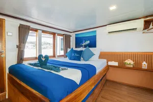 La Famille cabin on a Komodo boat with folded towel swan on blue bedding and sea view through the windows, Labuan Bajo