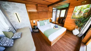 Luxurious phinisi bedroom with twin beds, green throw and sea-view windows on a 3D2N Komodo cruise in Labuan Bajo