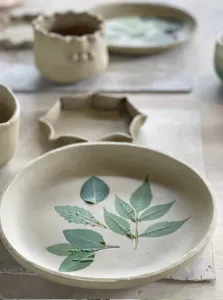 Hand-painted ceramic bowl with a botanical leaf design at Ilham Ceramic Studio in Langkawi, with other pieces in soft focus.