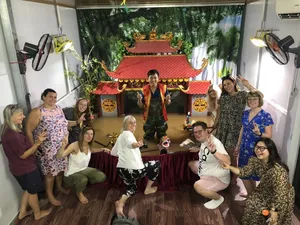 在河内,宾客围坐在水上木偶戏台旁,看木偶师表演,身后是灯光映照下的红顶布景