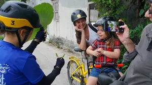 Bike guide taking a selfie with a mother and child beside yellow bicycles on a Mekong Island street near Ho Chi Minh City