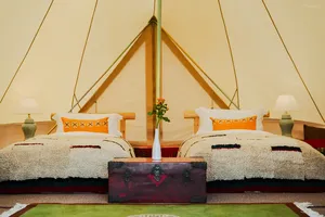 Cozy glamping tent interior at Ferme Liotard in Shangri-La with two beds, patterned cushions and a rug