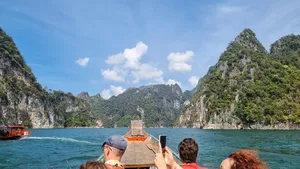 Travellers on a wooden long-tail boat passing limestone cliffs on a private Khao Sok day trip, Cheow Lan Lake