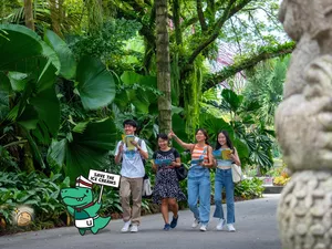 Group strolling along a lush garden path during a Singapore puzzle hunt for teams, carrying clue props and following the route