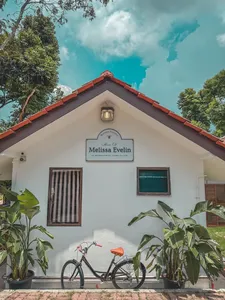 Exterior of a white bungalow with red roof tiles, a name sign and bicycle by potted plants at a Singapore farmstay by the sea