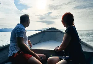 Couple relaxing at the front of a small boat during a Langkawi cruise, looking out over the sea at sunset