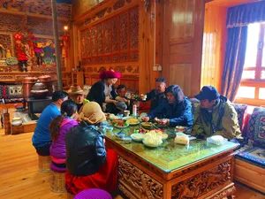 Tibetan home lunch in a warmly decorated room in Shangri-La, with travellers seated around dishes in a host-led meal