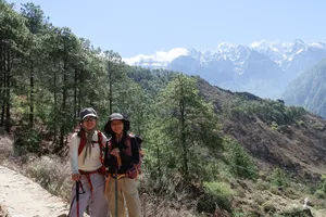 Two hikers on a dusty mountain footpath with pine trees and distant peaks during the Tiger Leaping Gorge high trail, Lijiang