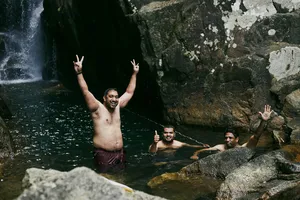 Smiling swimmers pose by a rocky pool under the falls on a Hoi An secret waterfall adventure in Vietnam
