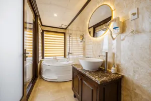 En-suite bathroom on the Oasis Bay Party Cruiser with a round bathtub, stone-tiled vanity and mirror lighting in Halong Bay