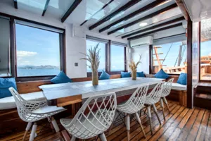 Private 3D2N Komodo cruise on a sleek white phinisi: bright lounge with dining table, sofas and windows overlooking Labuan Bajo