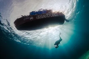 Diver silhouetted beneath a submerged shipwreck during a scuba dive, seen in Semporna’s clear ocean water