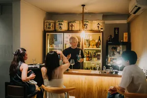 Host pouring rare sake for guests at a small bar counter, with labelled bottles and lantern light in Singapore — Singapore hidden gems