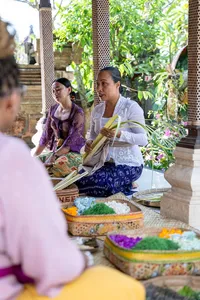 Balinese family and guests arranging canang sari offerings in a garden pavilion beside flower bowls, Ubud