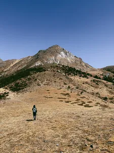 Solo hiker crossing a barren alpine slope toward a jagged peak on a guided hike of Jade Dragon Snow Mountain in Lijiang