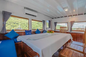 Onboard cabin with twin beds, blue cushions and large windows, for restful stays on a 3-day join-in Komodo boat trip in Labuan Bajo