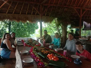 Guests enjoying a communal dinner on a long green table runner with flowers and candles under a thatched roof at Omunity Bali, Bali