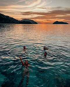 People floating and swimming at sunset in calm Andaman Sea water during Surin Island beach camping and snorkelling
