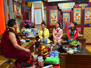 Lama in maroon robes leads a tea-time conversation as travellers sit by a decorated table of pots in Shangri-La