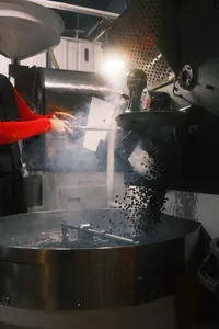 Workers operating a hot metal pressing machine in Hoi An, with smoke and paper slips falling as steam fills the chamber