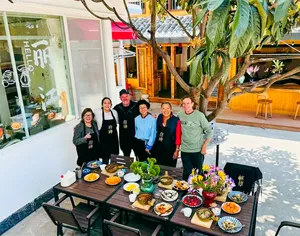 Travellers gathered around a decorated outdoor table of dishes at the end of a Lijiang Yunnan cooking experience in a courtyard
