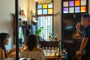 Guests seated at a wooden tasting table, swirling small-batch whisky in a hidden home bar in Katong, Singapore under candlelight