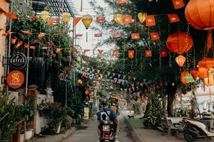 Gang bercahaya lentera dengan bendera Vietnam saat skuter Hoi An Backroad Tours melaju melewati jalan yang dihias di Hoi An