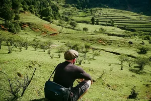 Traveller sitting on a grassy lookout above terraced countryside around Lijiang, Yunnan, on a Yi and Naxi village trek