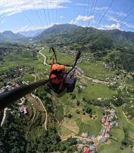 View from a paraglider seat as the canopy lines stretch over a valley with a winding river and village clusters in Sapa