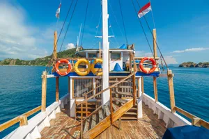 La Famille Komodo boat’s front deck with orange lifebuoy rings and sail flags, mast over open water on Labuan Bajo