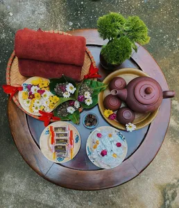 Top-down view of a round tray tea spread near Hanoi: purple teapot with cups, flowers, and greenery for a herbal brew