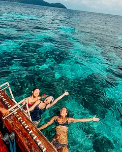People swimming and snorkelling in clear turquoise water from a boat near Surin Island, with dark forested hills in view