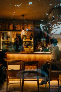 Warm-lit sake bar interior with rows of bottles on wooden shelves and pendant light, in SakeMama’s tucked-away Singapore shop