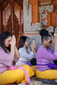 Attendees seated in a Balinese temple praying with hands raised together during canang sari ceremony, Ubud