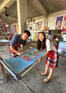 Batik workshop at Five Arts Studio in Keliki, two people paint colourful motifs on fabric stretched on a batik frame in Ubud