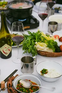Camp dining table set for a Shangri-La caravan journey, with wine, bowls of soup and fresh greens on white plates