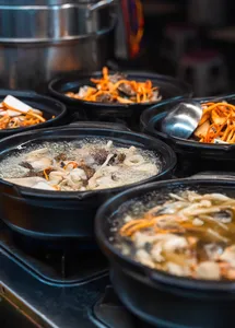 Hotpots simmering in metal pans with vegetables and fish for tasting at a local Lijiang street food stop