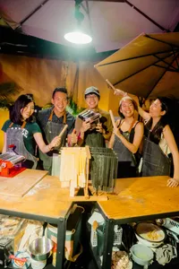 Friends making fresh pasta by hand at workshops in Singapore, chatting as lunch is served outdoors under warm lights