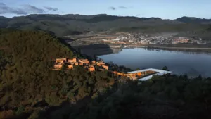 Pemandangan udara Linden Centre eco retreat di Shaxi, Dali, dengan bangunan beratap oranye di tepi danau tenang dan dikelilingi pegunungan
