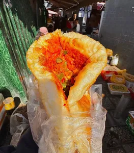 Folded, golden flatbread with bright red chilli filling wrapped in paper at a Lijiang street food stall