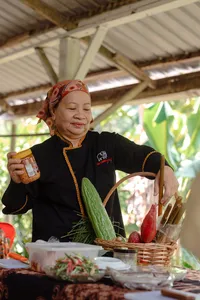 Indigenous Sabahan family cook holding a spice jar at a wooden table outdoors in Kota Kinabalu, Sabah