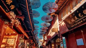 Narrow wooden alley in Lijiang Old Town strung with colourful paper parasols overhead, with shop signs lining both sides