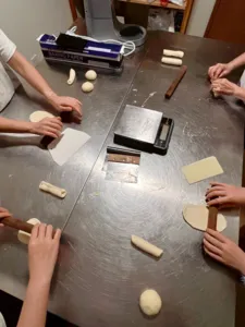Participants shaping smaller shio pan rolls at The Daily Staples in Singapore, with baking paper, dough pieces and boards laid on the table