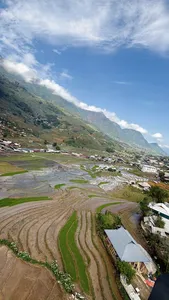 Patchwork rice terraces and small houses stretch across a mountain valley with cloud overhang, Sapa