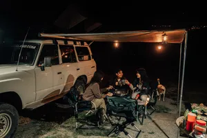 People sharing dinner at a lantern-lit wild campsite beside a 4x4 van during a Borneo Overland roadtrip in Sabah
