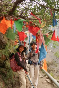 Trekking on the Tiger Leaping Gorge trail in Lijiang with colourful prayer flags overhead as hikers climb a rocky path