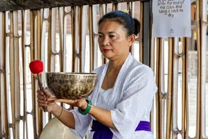 ADDA Yoga practitioner holding a singing bowl with a wooden mallet in Canggu, Bali during rooftop sound healing