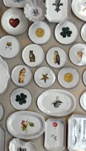 Assortment of small decorative ceramic plates with animal, flower and sun motifs arranged in rows on a display table